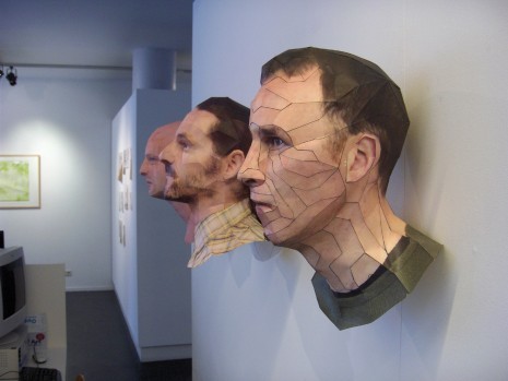 [photo of three papercraft heads, stuck to a wall]